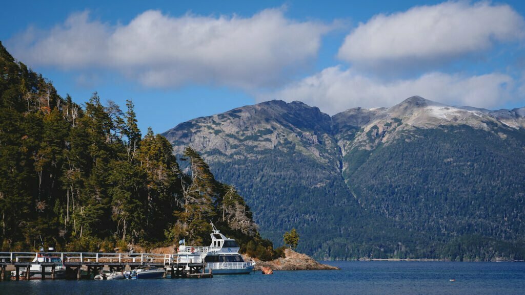 A boat sits next to a dock in the town of Villa La Angostura with mountain, lake and forest views. 