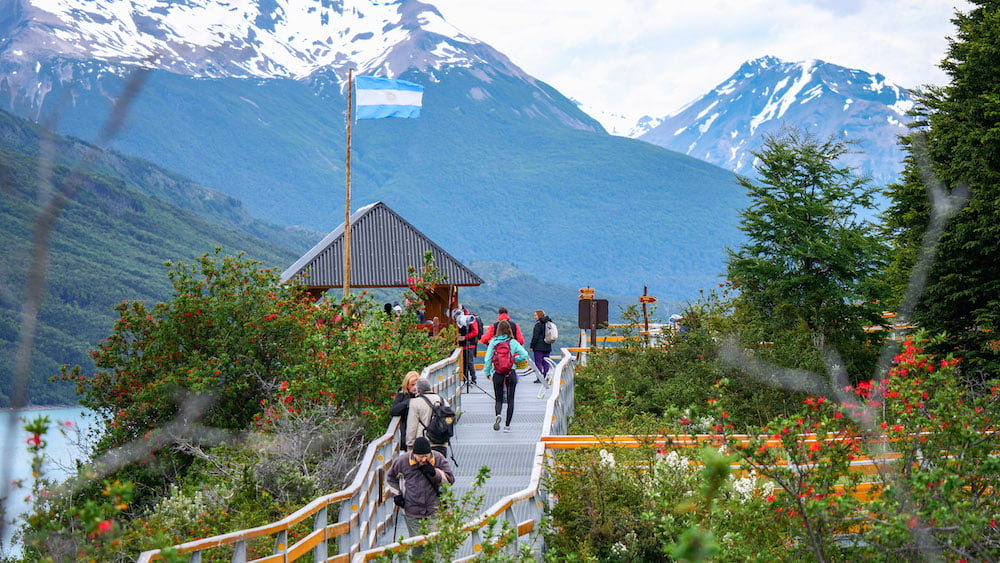 Visitors walk the boardwalks of Los Glaciares National park with mountains in the background. 