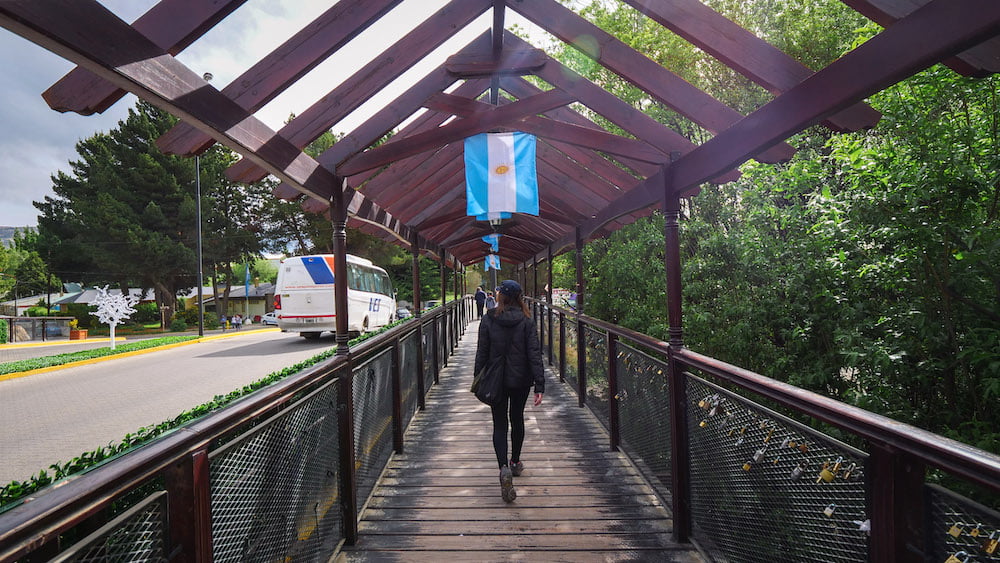 Walking across a covered wooden bridge in El Calafate with Argentine flags hanging overhead 