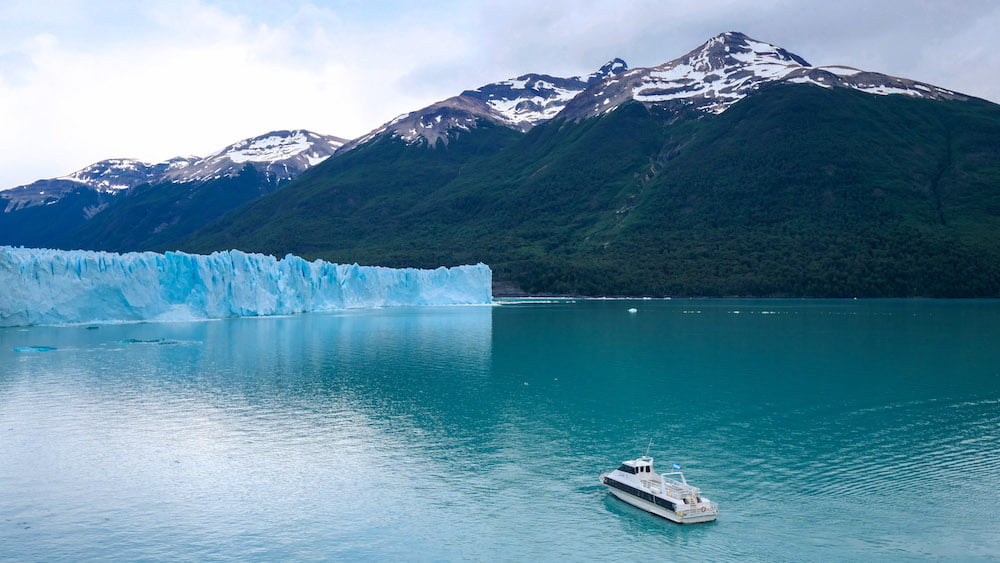 Small boat cruising Lago Argentino with Perito Moreno Glacier in the background.
