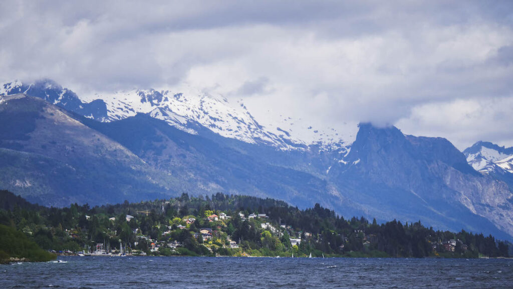 The views while walking along Bariloche's lakeshore feature forested hills and mountains covered in snow.