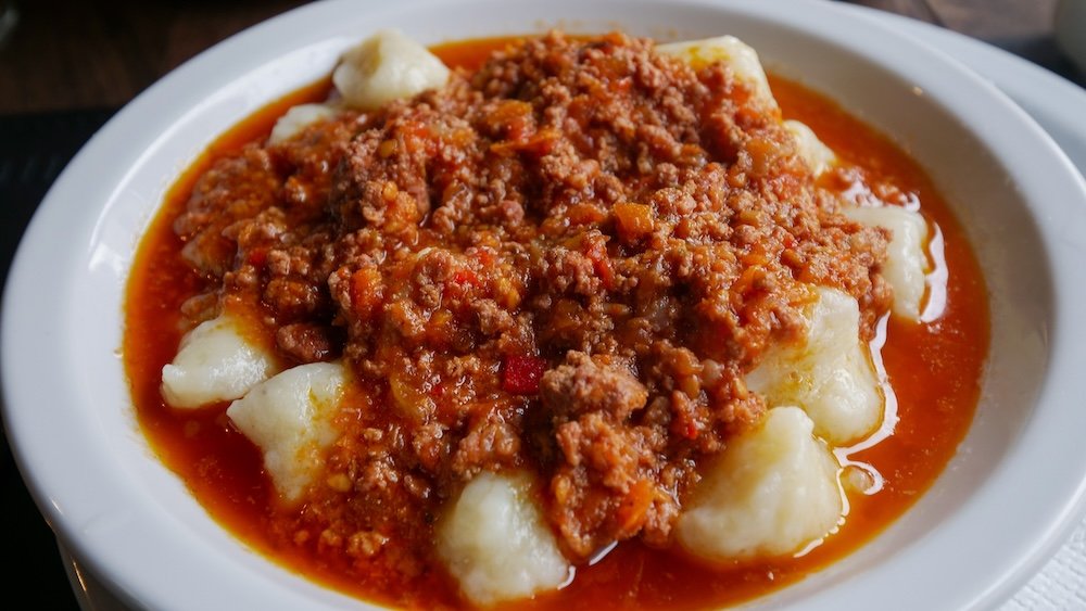 Plate of ñoquis served in a tomato bolognese sauce.