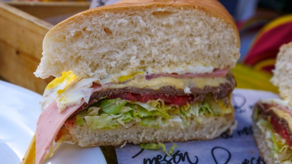 Lomito is a thin steak sandwich with lettuce, tomato, ham, cheese, and a fried egg served in a fluffy bread.