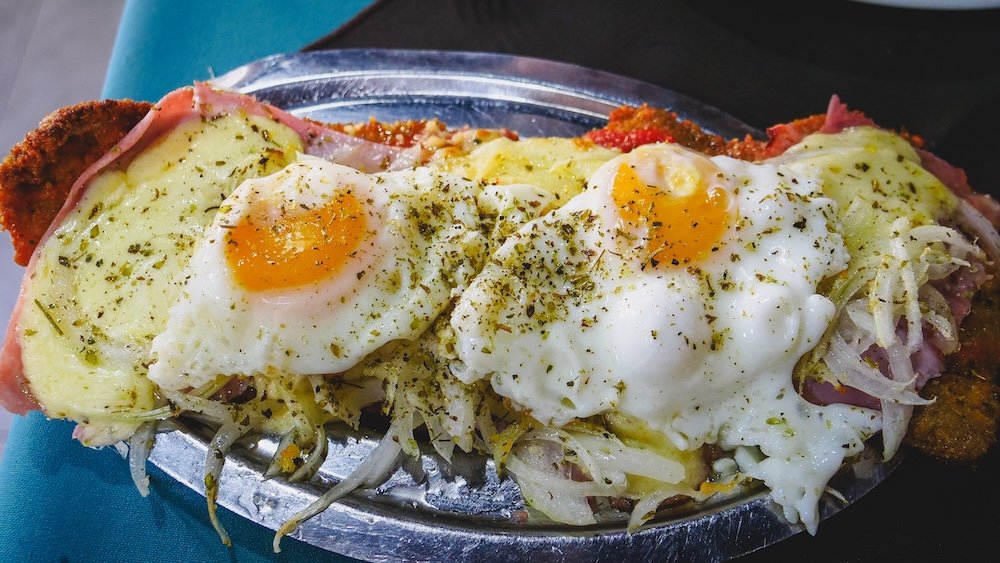 Milanesa al caballo is served with two fried eggs on top.