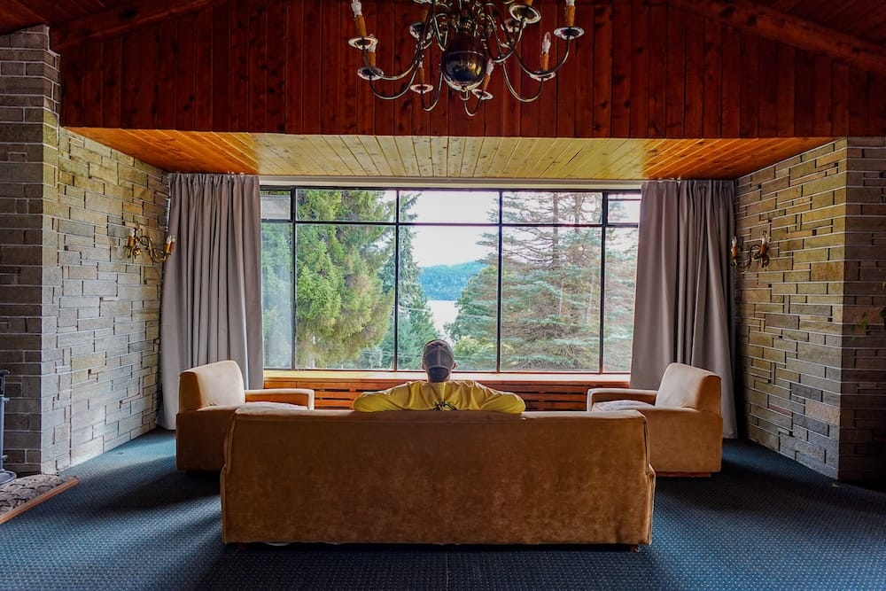 Samuel sitting in the living room of Gran Hotel Panamericano in front of large window with forest and lake views.