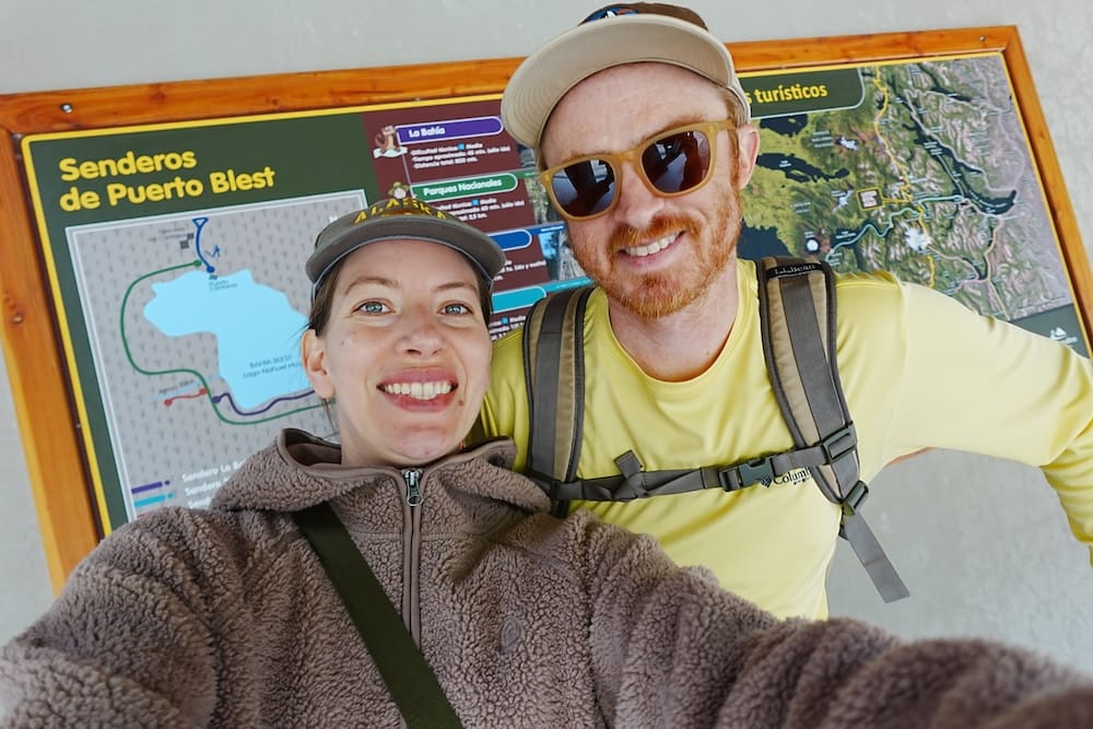 Samuel and Audrey smiling in front of the Puerto Blest trail map showcasing the different hikes.