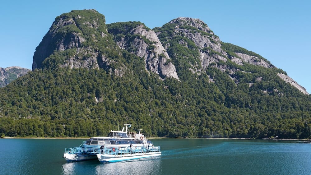 Catamaran cruising into Puerto Blest. The waters are turquoise and there are mountains in the background.